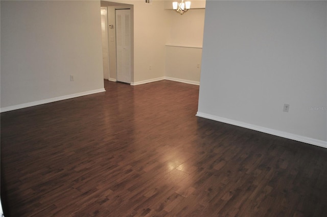 empty room with dark hardwood / wood-style flooring and a notable chandelier