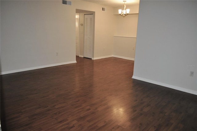 empty room with dark wood-type flooring and a chandelier