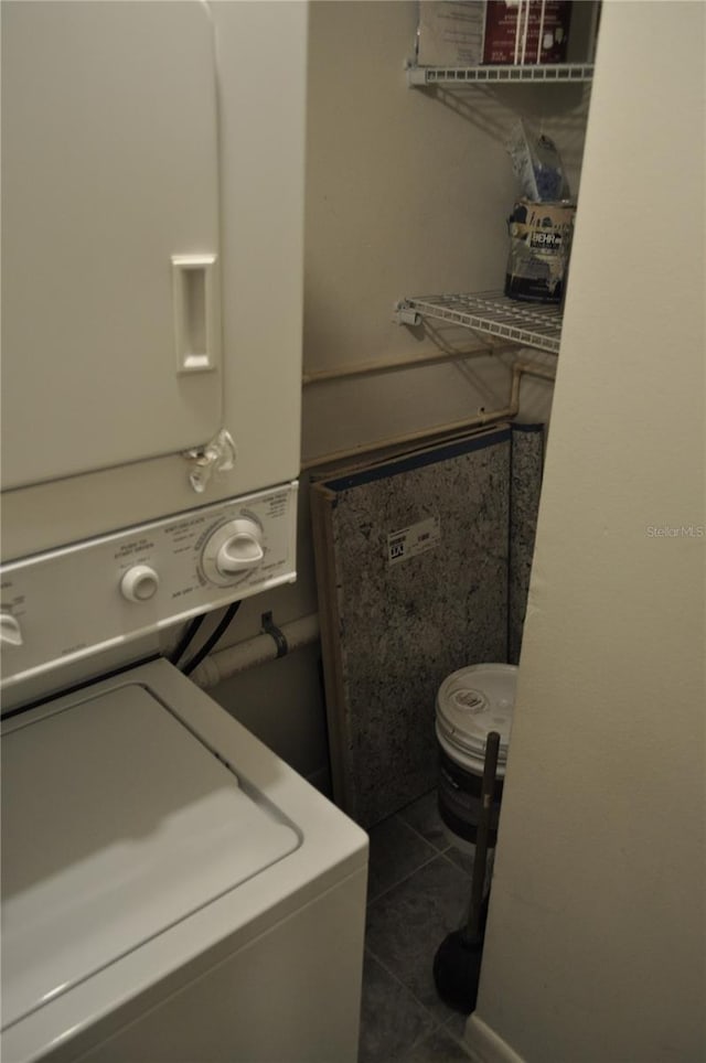 washroom featuring stacked washer / drying machine and dark tile patterned flooring