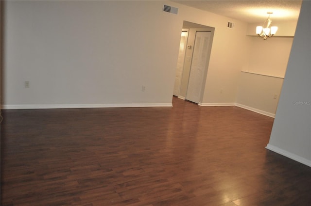 spare room with an inviting chandelier, dark hardwood / wood-style floors, and a textured ceiling