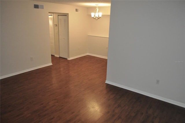 empty room with dark wood-type flooring and an inviting chandelier