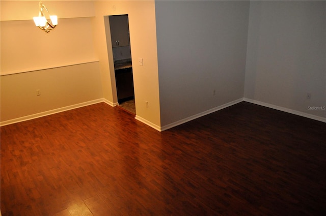 empty room with dark hardwood / wood-style flooring and an inviting chandelier