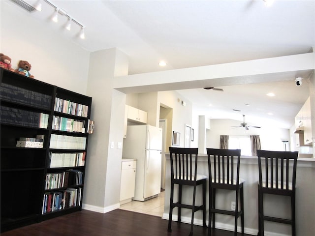 kitchen featuring a kitchen breakfast bar, light wood-type flooring, ceiling fan, white refrigerator, and white cabinetry