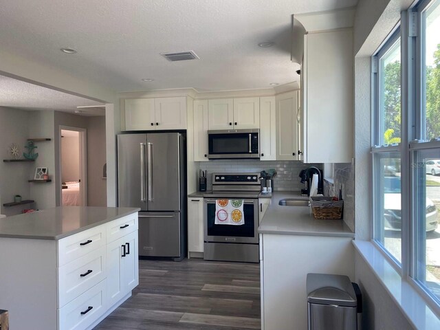 kitchen with a kitchen island, backsplash, stainless steel appliances, white cabinets, and dark wood-type flooring