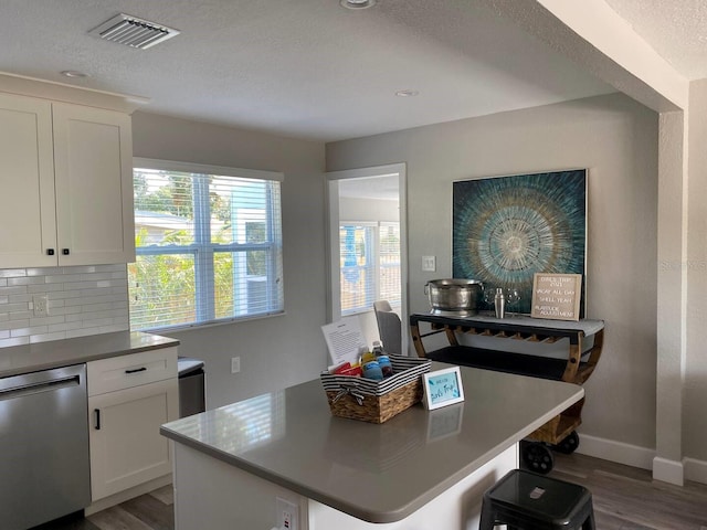 kitchen featuring decorative backsplash, white cabinets, hardwood / wood-style floors, stainless steel dishwasher, and a center island