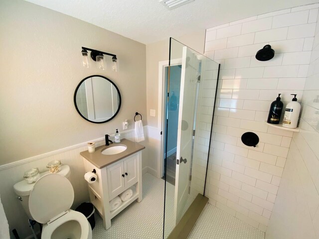 bathroom with toilet, tile patterned flooring, vanity, a tile shower, and a textured ceiling