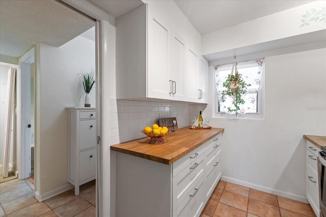 kitchen featuring tasteful backsplash, butcher block counters, stainless steel range, white cabinets, and light tile patterned floors