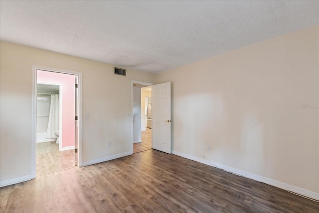 unfurnished bedroom with hardwood / wood-style floors, ensuite bathroom, and a textured ceiling