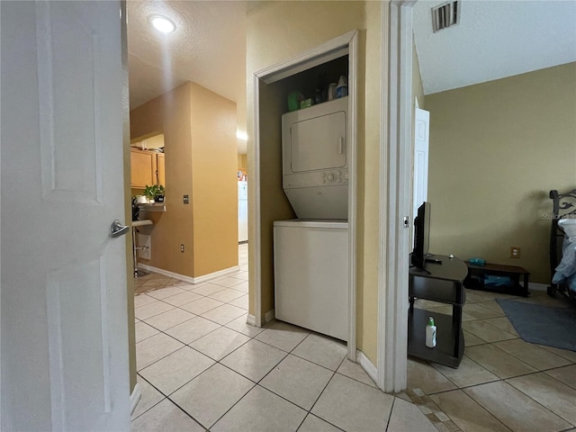 washroom with stacked washer / drying machine and light tile patterned floors