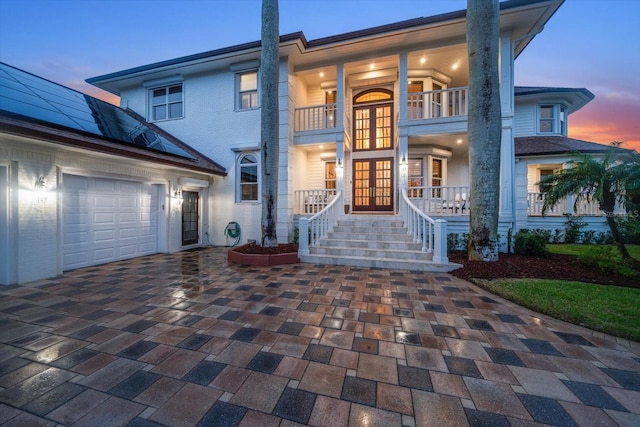 view of front facade with a garage, french doors, decorative driveway, and roof mounted solar panels