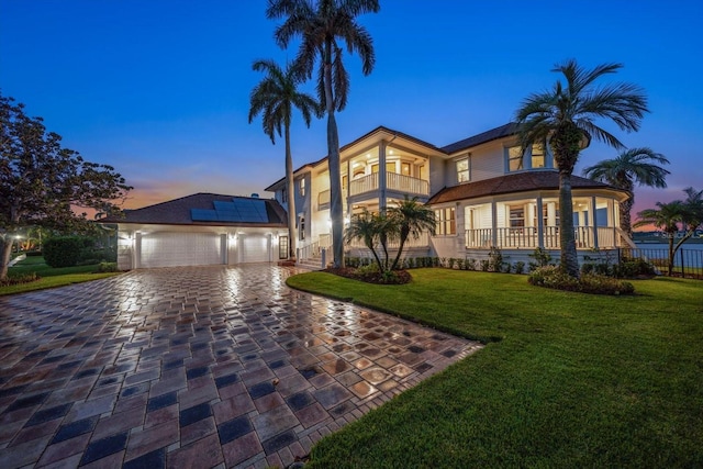 view of front of home featuring a lawn, a balcony, decorative driveway, roof mounted solar panels, and a porch