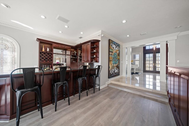 bar with light wood finished floors, visible vents, bar, ornamental molding, and french doors