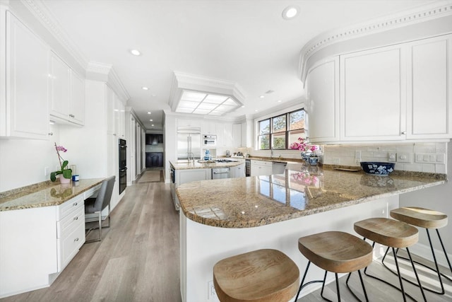 kitchen featuring stone counters, a peninsula, white cabinetry, backsplash, and a kitchen bar