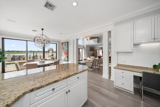 kitchen with white cabinets, visible vents, decorative light fixtures, and built in study area