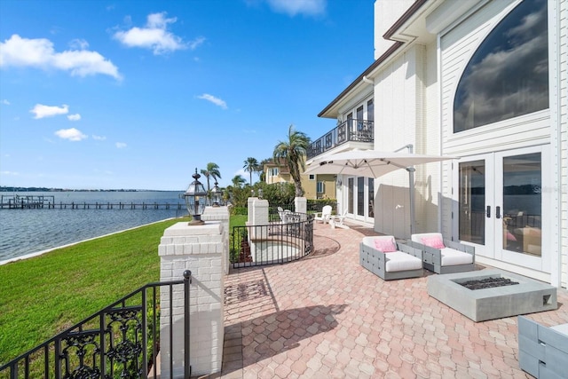 view of patio / terrace with a water view, a balcony, a fire pit, and french doors