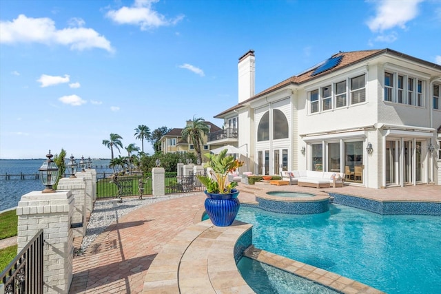 rear view of house with a patio, a chimney, a water view, roof mounted solar panels, and fence