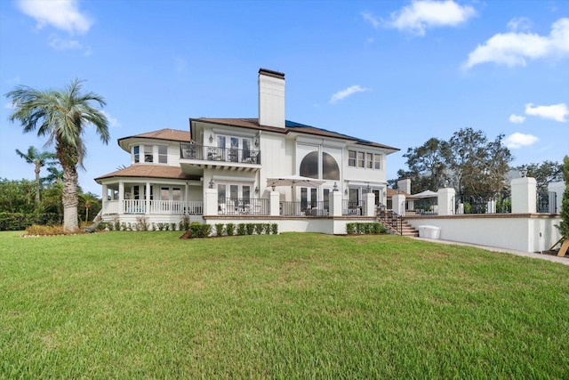 back of property featuring a chimney, a lawn, and a balcony