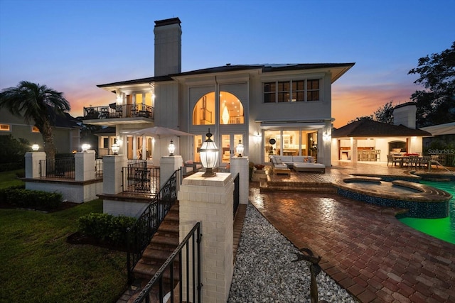 back of house featuring a chimney, a pool with connected hot tub, a patio area, a balcony, and an outdoor living space