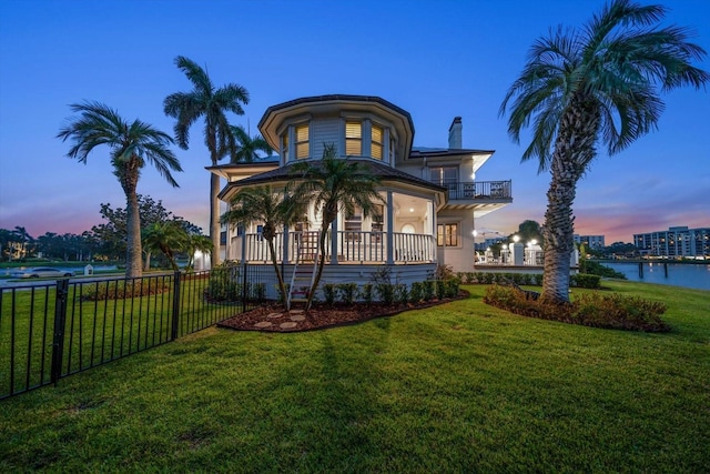 view of front facade featuring a lawn, a water view, fence, and a balcony