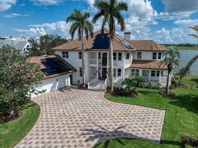 view of front of property featuring decorative driveway, a chimney, a water view, a front yard, and a balcony