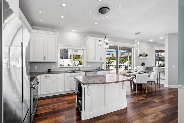 kitchen featuring stainless steel appliances, white cabinets, dark stone counters, and decorative light fixtures