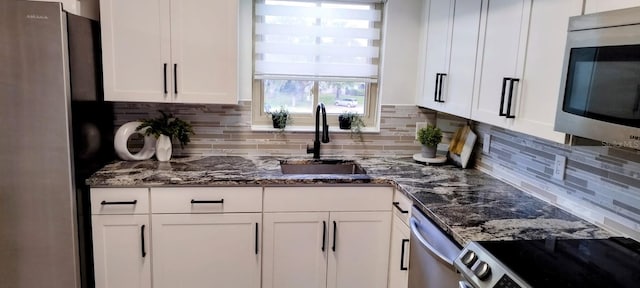 kitchen with dark stone counters, white cabinets, sink, decorative backsplash, and stainless steel appliances