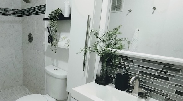 bathroom with backsplash, vanity, tiled shower, and toilet