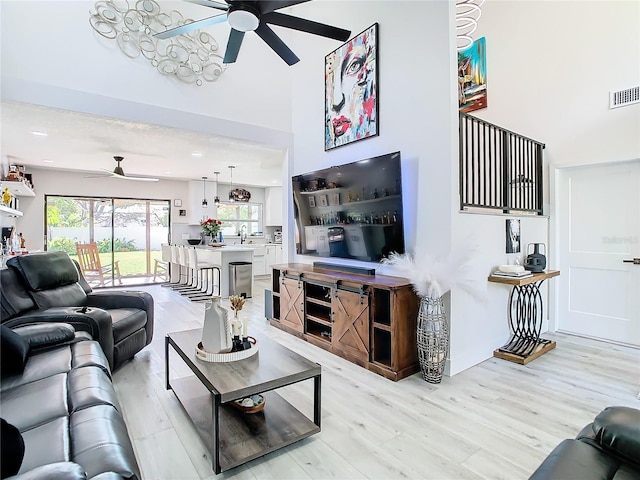 living room with a towering ceiling, sink, light wood-type flooring, and ceiling fan