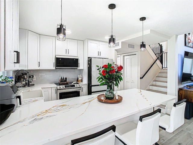 kitchen with kitchen peninsula, white cabinets, hanging light fixtures, appliances with stainless steel finishes, and light wood-type flooring