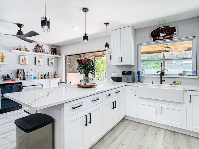 kitchen featuring kitchen peninsula, white cabinets, light wood-type flooring, pendant lighting, and sink