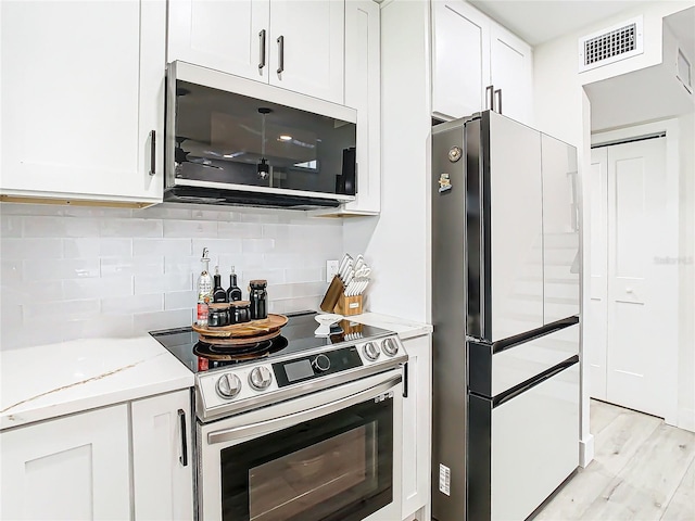 kitchen featuring backsplash, white cabinetry, light hardwood / wood-style floors, stainless steel appliances, and light stone counters