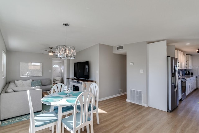 dining room with ceiling fan with notable chandelier and light hardwood / wood-style flooring