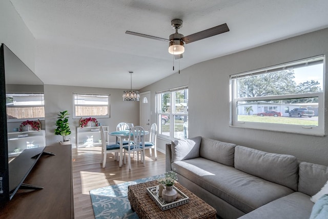 living room with lofted ceiling, a healthy amount of sunlight, light wood-type flooring, and ceiling fan with notable chandelier