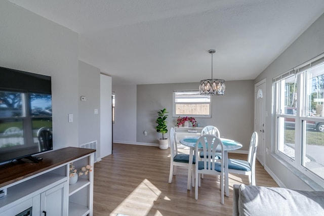 dining room with a healthy amount of sunlight, vaulted ceiling, a chandelier, and light hardwood / wood-style flooring