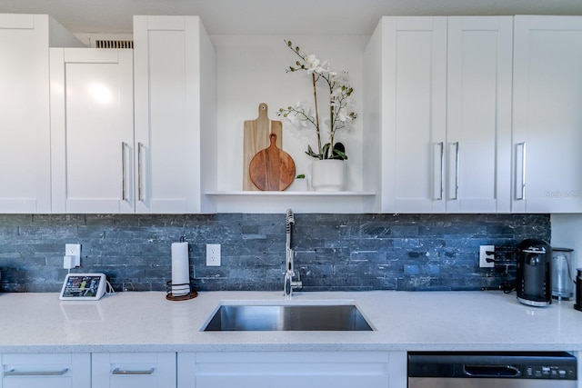 kitchen featuring tasteful backsplash, stainless steel dishwasher, sink, white cabinets, and light stone counters