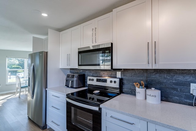 kitchen featuring white cabinetry, hardwood / wood-style flooring, appliances with stainless steel finishes, tasteful backsplash, and light stone countertops