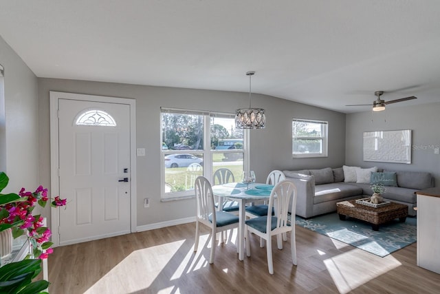 dining space featuring ceiling fan with notable chandelier, vaulted ceiling, and light wood-type flooring