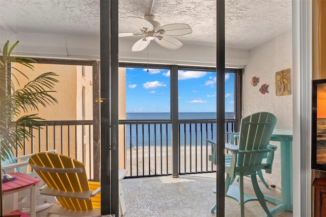 sunroom featuring ceiling fan, a water view, and a view of the beach