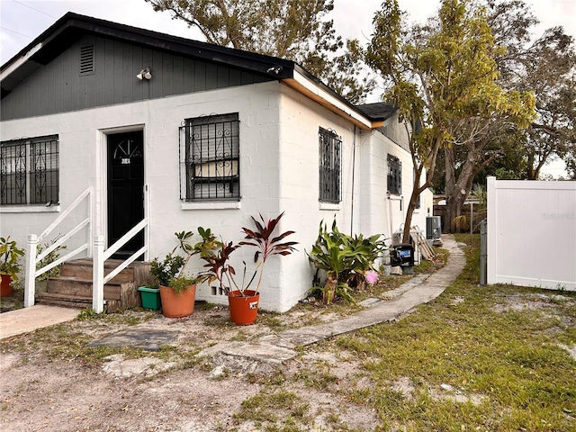 view of side of home with entry steps, central AC, concrete block siding, and fence