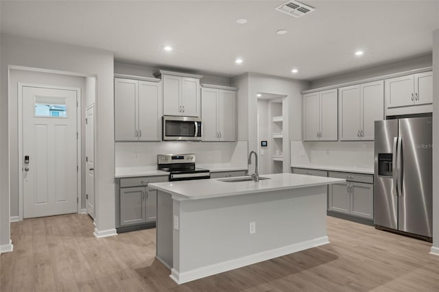 kitchen featuring stainless steel appliances, a center island with sink, sink, light wood-type flooring, and gray cabinets