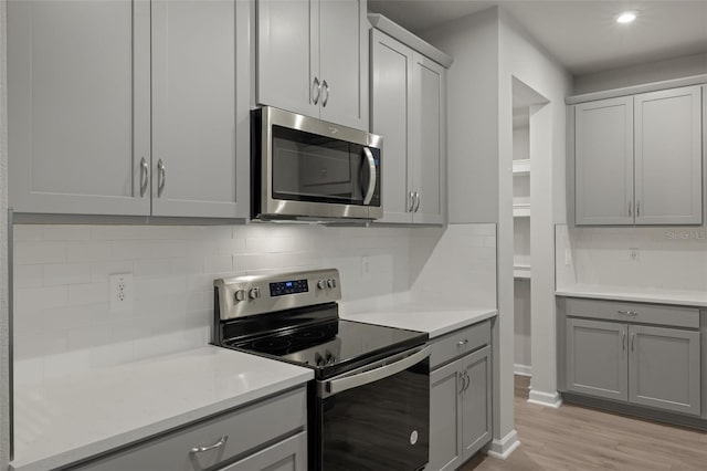 kitchen with gray cabinets, appliances with stainless steel finishes, light wood-type flooring, and tasteful backsplash