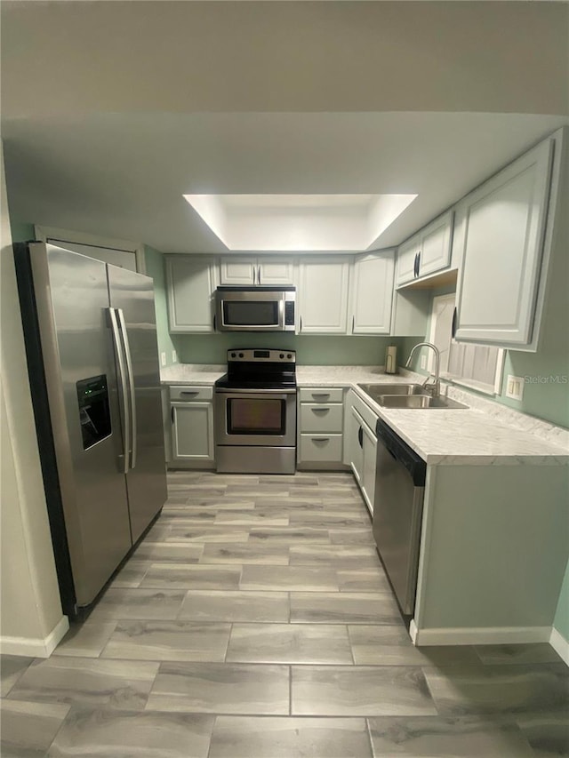 kitchen featuring a tray ceiling, stainless steel appliances, sink, and light wood-type flooring