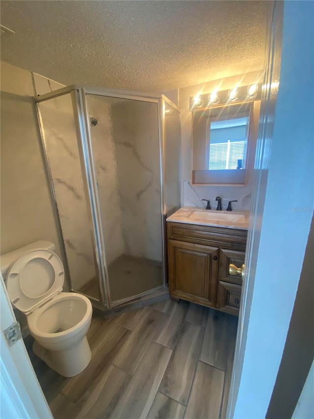 bathroom featuring a shower with door, a textured ceiling, wood-type flooring, toilet, and vanity