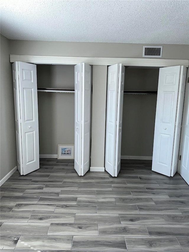 unfurnished bedroom featuring light hardwood / wood-style floors, a textured ceiling, and two closets