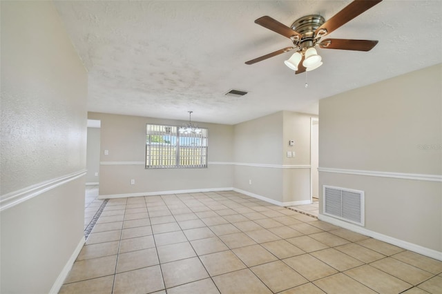 tiled spare room featuring a textured ceiling and ceiling fan with notable chandelier