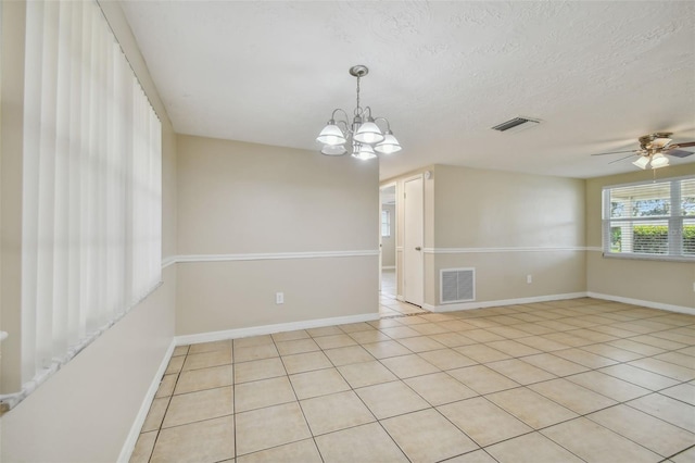 empty room with a textured ceiling, light tile patterned floors, and ceiling fan with notable chandelier