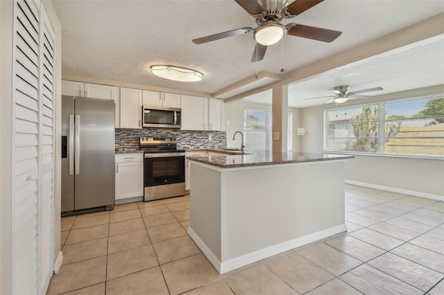 kitchen with white cabinetry, stainless steel appliances, tasteful backsplash, and dark stone countertops