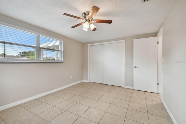 unfurnished bedroom with a closet, a textured ceiling, light tile patterned floors, and ceiling fan