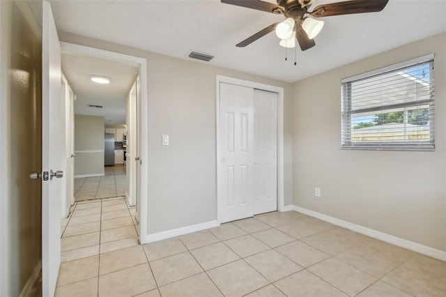 unfurnished bedroom featuring a closet, ceiling fan, stainless steel refrigerator, and light tile patterned floors