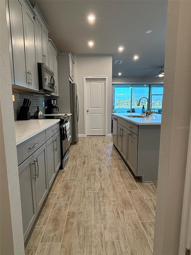 kitchen featuring gray cabinetry, stainless steel appliances, sink, light wood-type flooring, and tasteful backsplash